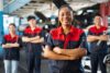 Employees stand in the workshop with their arms folded and smiling